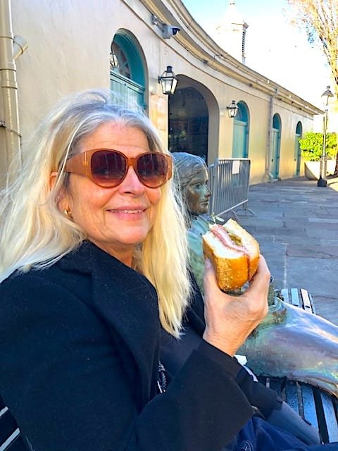 alt=" Nina Zapala in New Orleans eating a muffuletta sandwich."